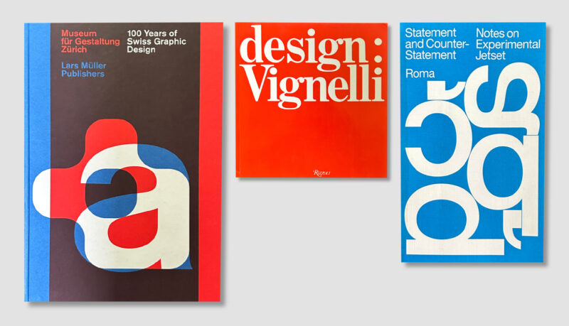 Overhead view of three design books, including a Vignelli title, with brown, red and blue covers.