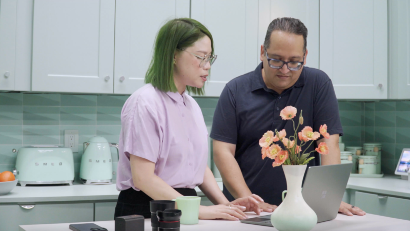 Two people looking at a laptop together in a bright kitchen.
