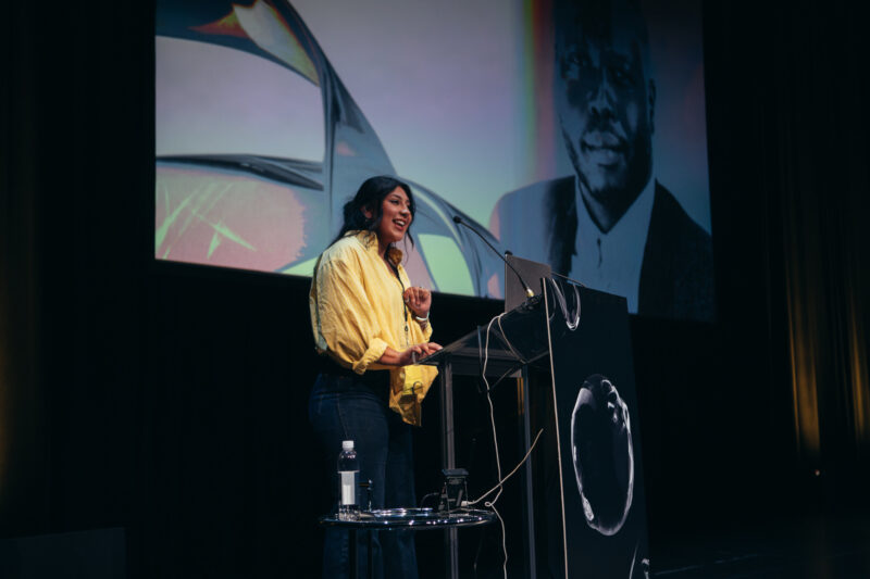 Bella Sanchez on-stage at DesignThinkers 2025 introducing a speaker.